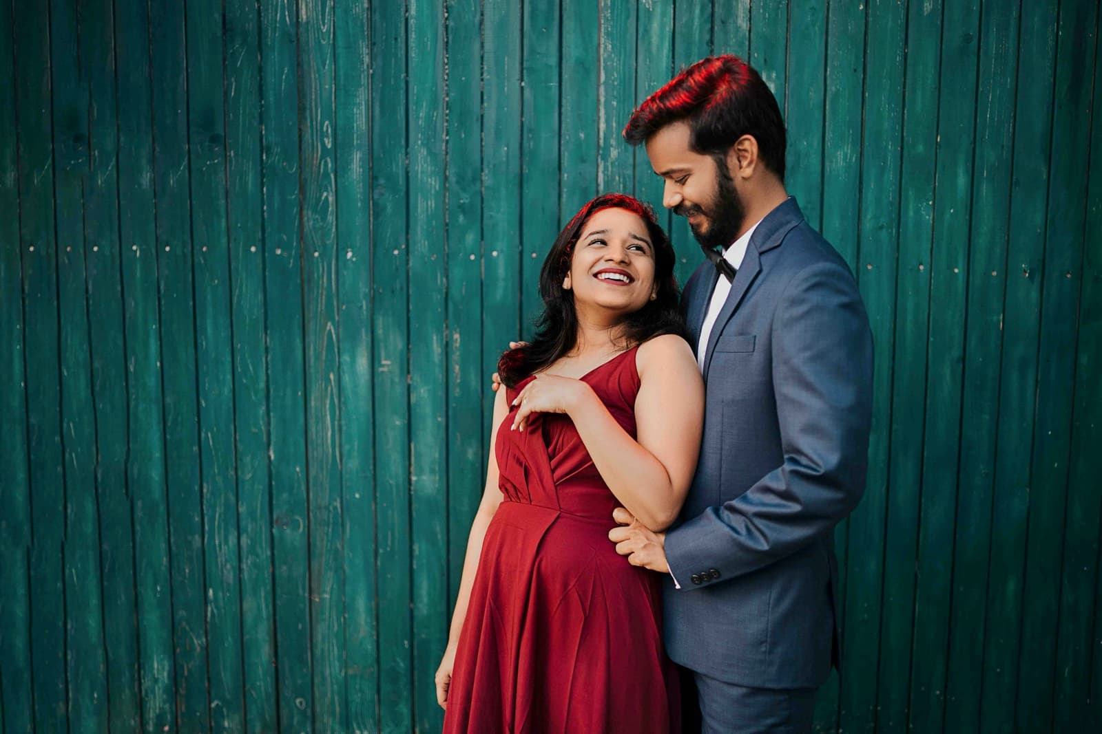 Couple against teal wooden background with woman in red dress