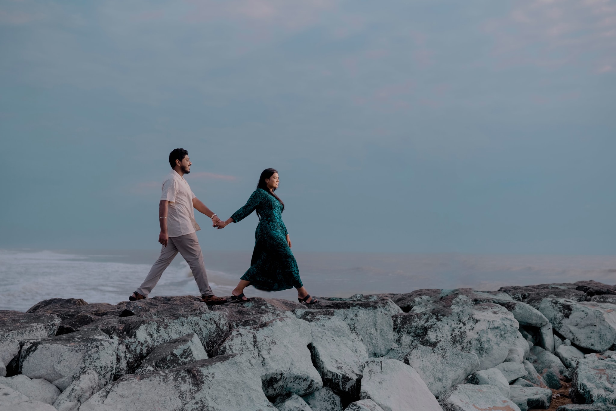 Couple walking hand-in-hand along a rocky shoreline at dusk, showcasing our professional color grading and mood enhancement