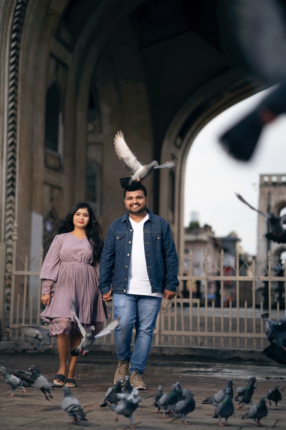 Couple walking hand-in-hand surrounded by pigeons at a historic location, showcasing our candid photography style