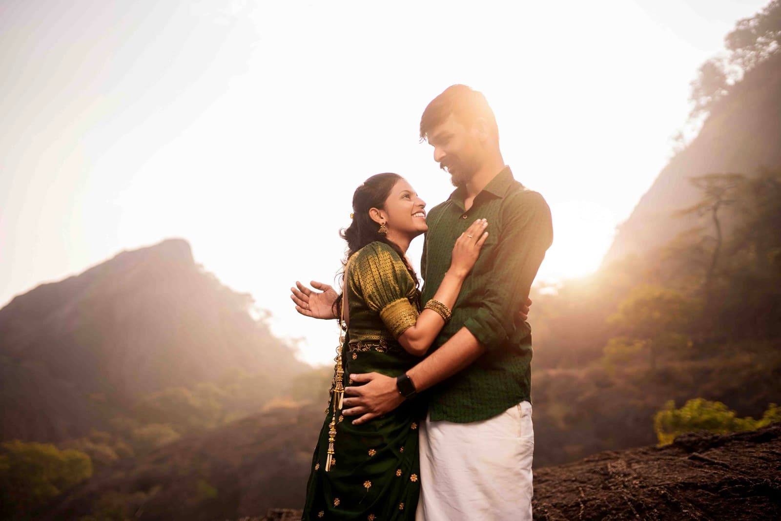 Couple in traditional South Indian attire embracing at sunset with mountains in background