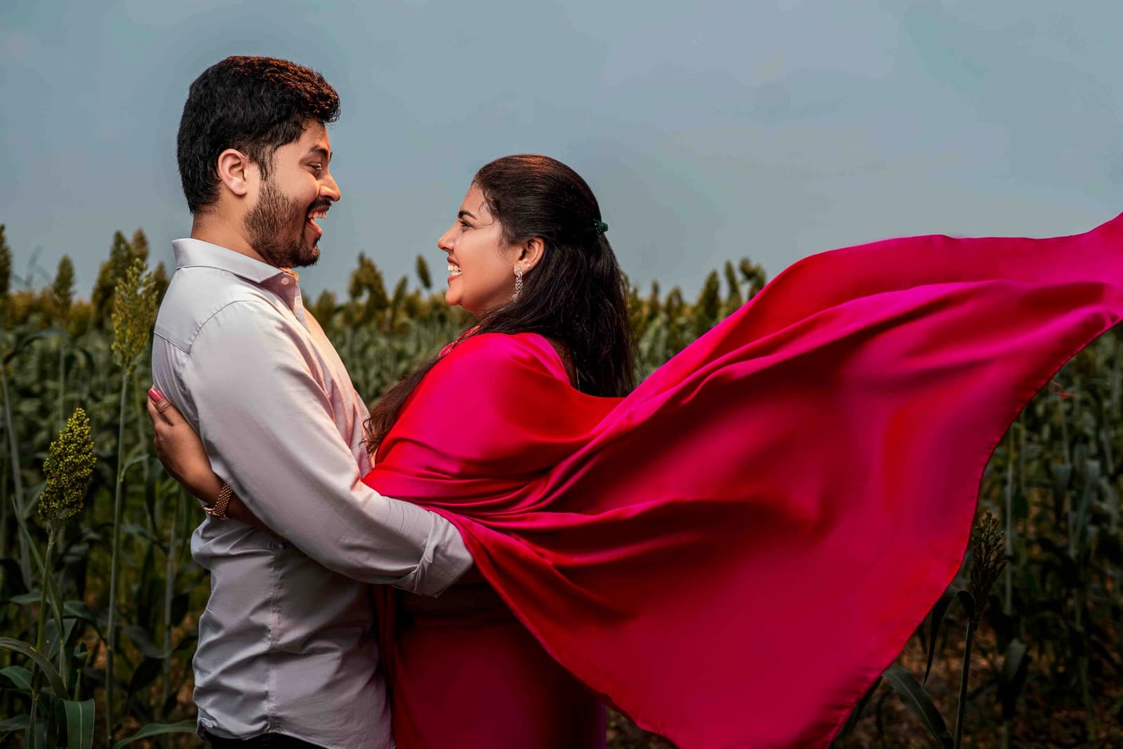 Couple with woman in flowing red dress in a field with fabric dramatically flowing