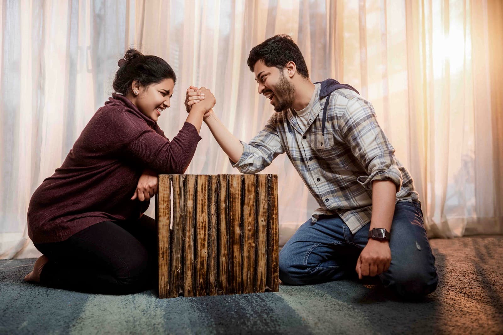 Playful couple arm wrestling on a wooden box in casual indoor setting