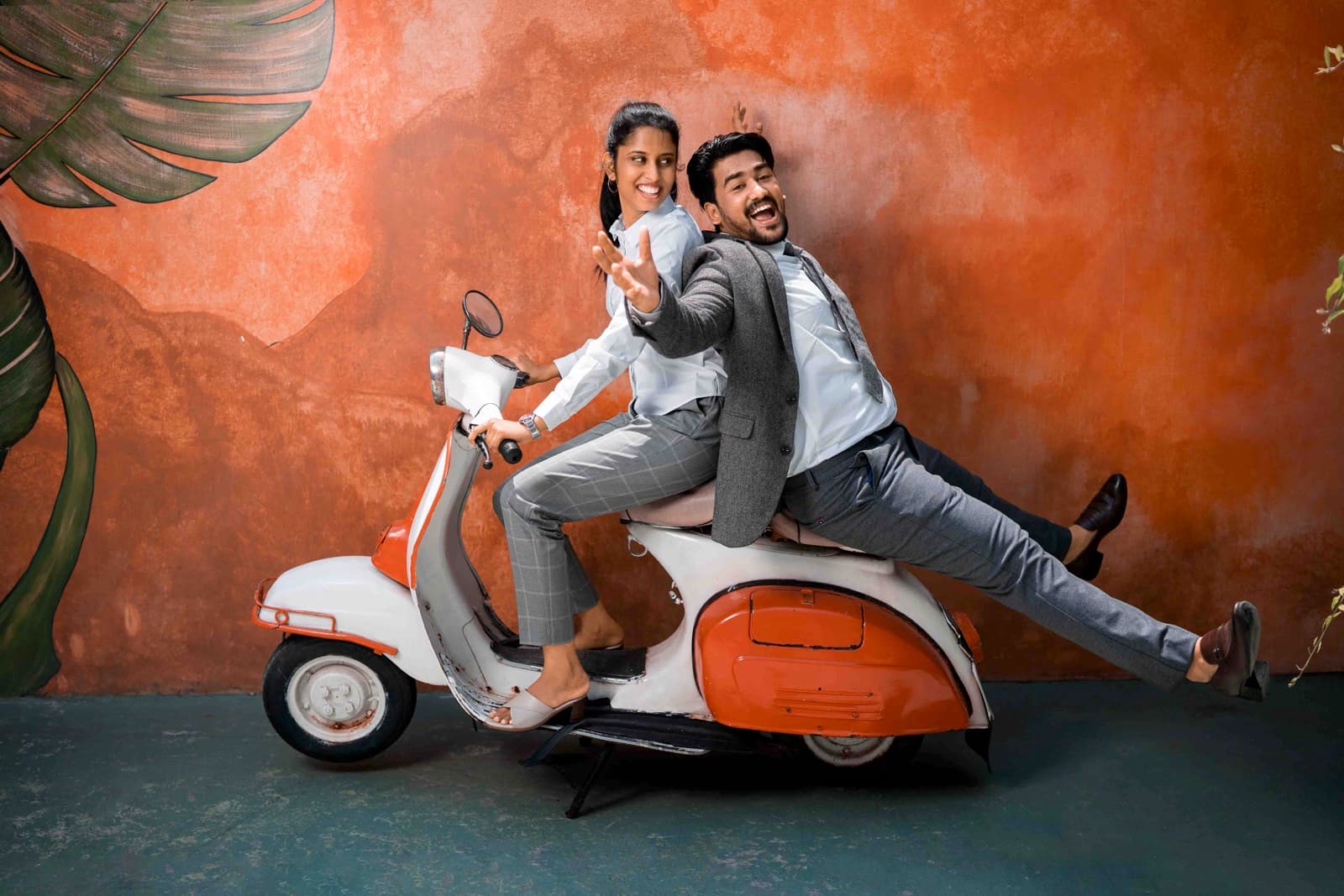 Fun couple on a vintage Vespa scooter against an orange wall