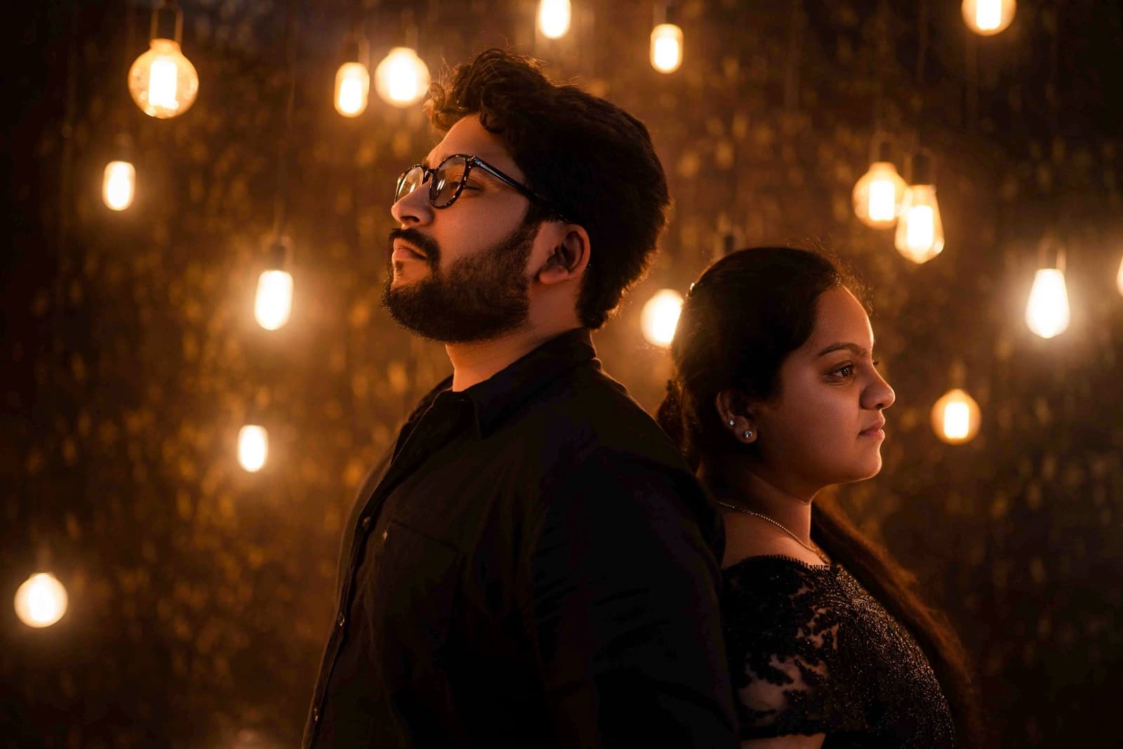 Couple in formal black attire with hanging string lights in the background