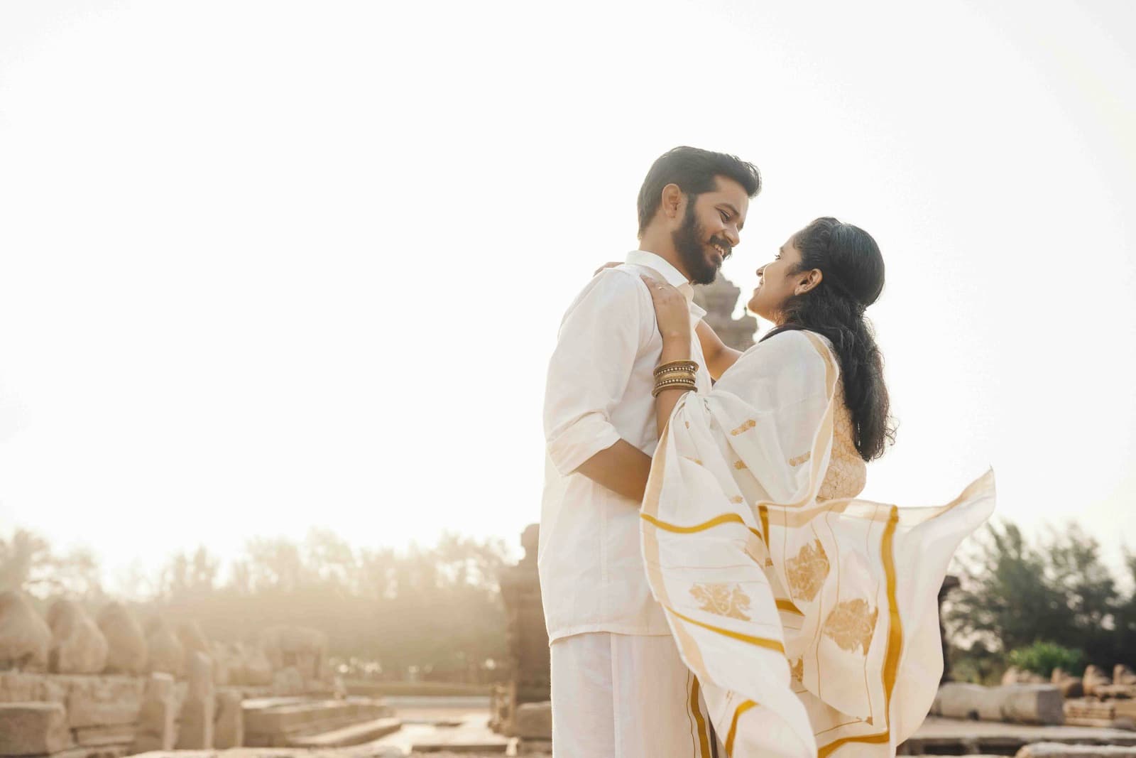 Couple in traditional white Indian attire with gold accents at a historical site